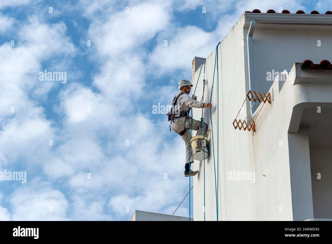 Seilzugangsabseiler, Gebäudereparaturen und Maler tragen an der Seite eines Gebäudes einen vollen Sicherheitskabelbaum Stockfoto