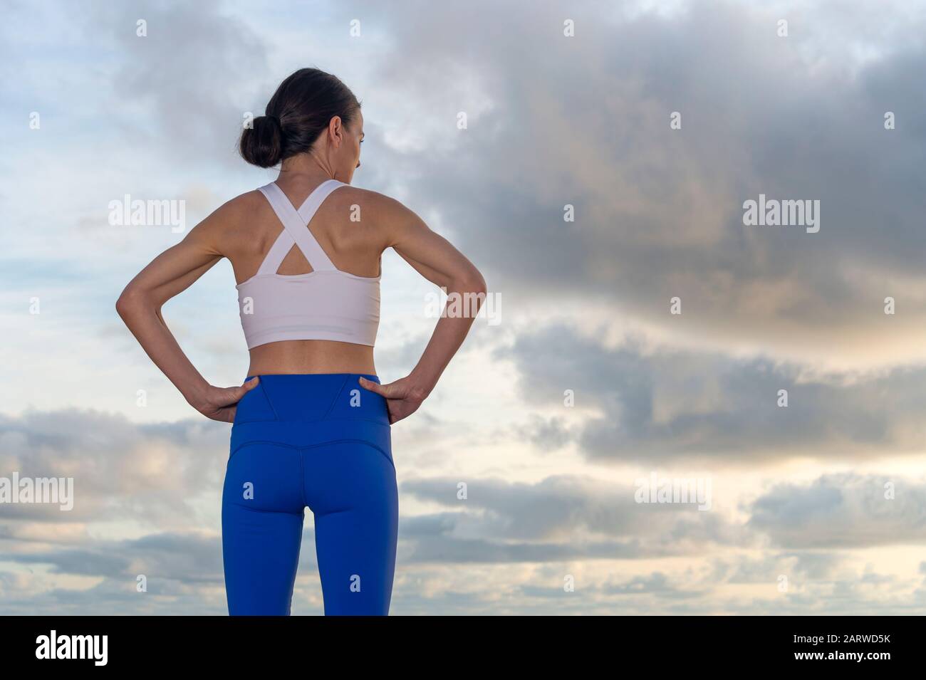 Rückansicht einer sportlichen Frau mit den Händen an der Hüfte, die nach dem Training, Sonnenaufgang und Sonnenuntergang ruht. Stockfoto