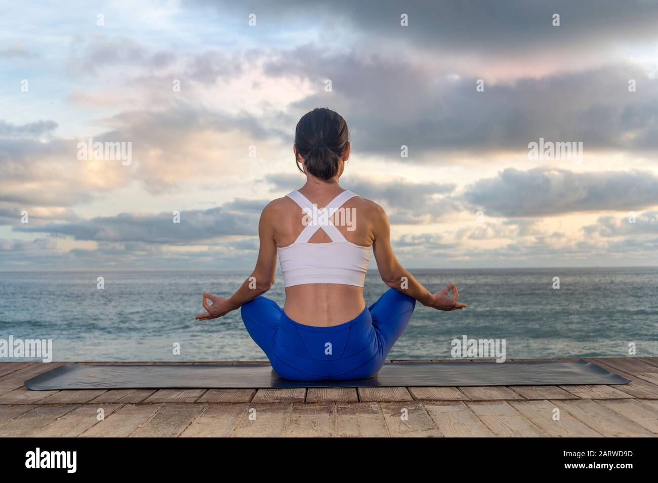 Frau, die Yoga praktiziert, in Der Easy Seat Übung sitzt, Sukhasana Pose, ausarbeitet, Meditationssitzung. Rückansicht mit Meeresgrund Stockfoto