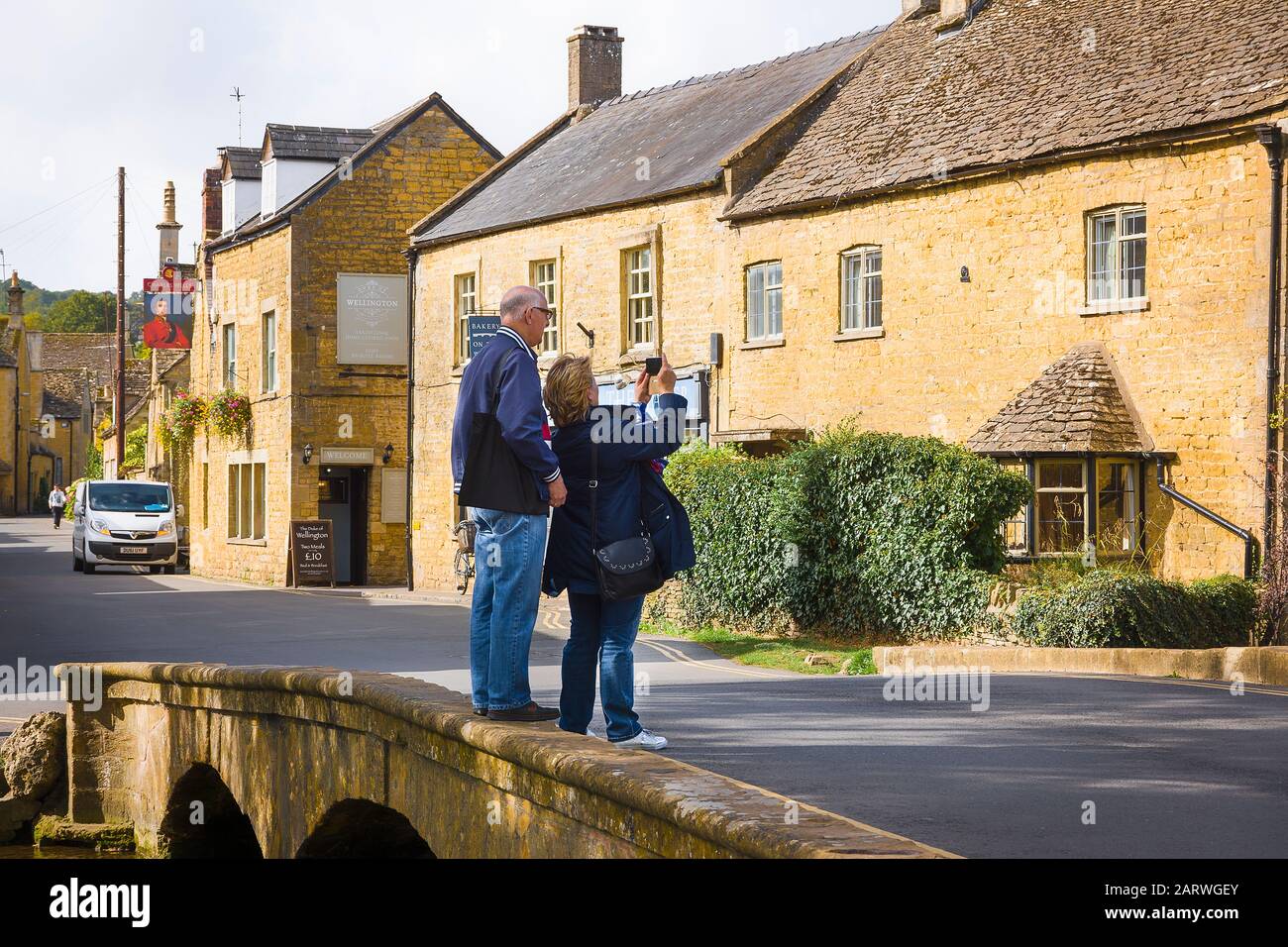 Ein paar Besucher, die ein selfie nehmen, während sie gefährlich am Rande einer Straßenbrücke über den River Windrush in Bourton auf dem Wasser in Gloucé stehen Stockfoto