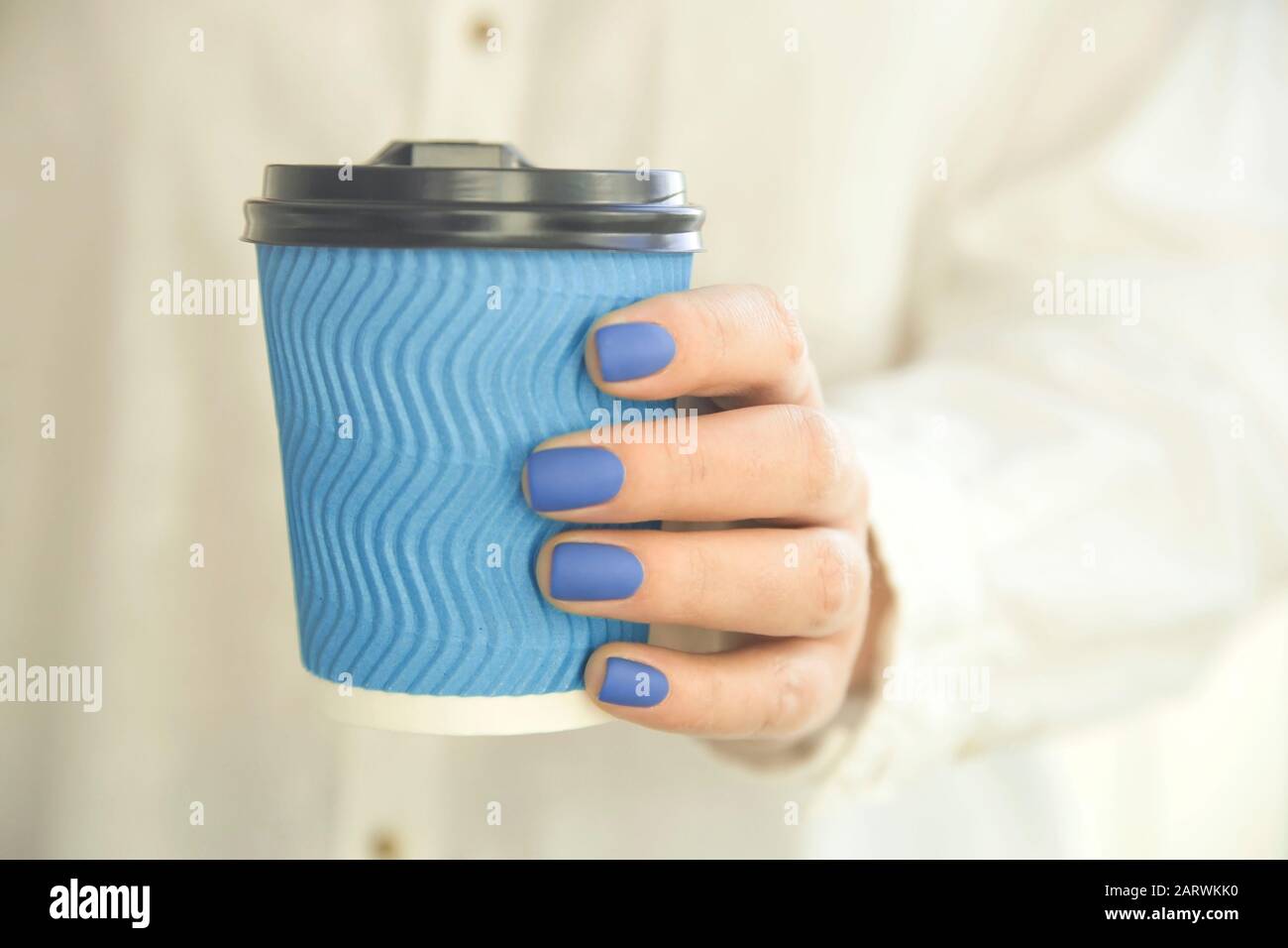 Papierblaues Glas für Kaffee in den Händen einer Frau mit einer blauen Maniküre in matt. Stockfoto