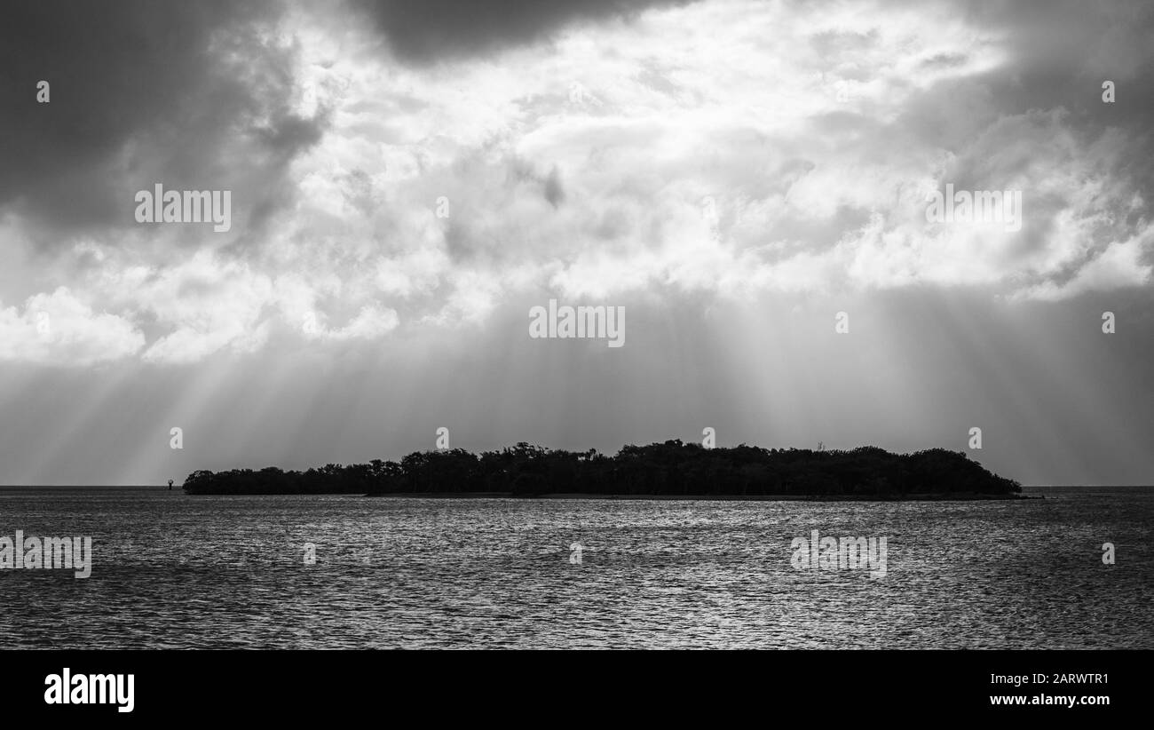 Graustufenaufnahme einer Insel im Meer mit einem Sonnenstrahl am Himmel Stockfoto