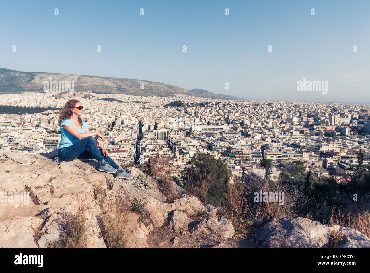 Junge hübsche Frau blickt auf die Stadt Athen, Griechenland. Schöner Erwachsenen-Tourist entspannt mit Blick auf Athen im Sommer. Attraktive Person steht im Hintergrund Stockfoto