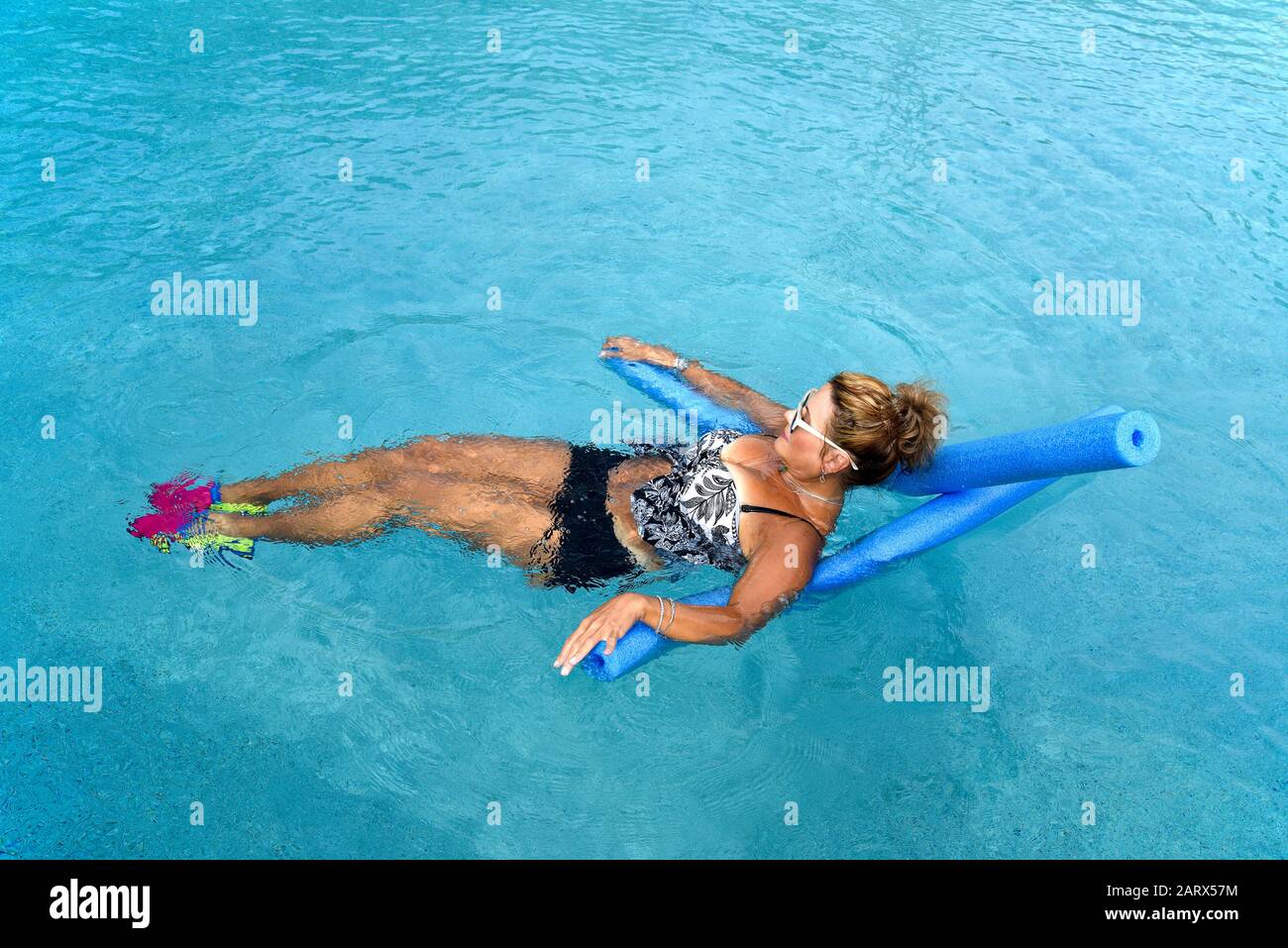 Eine reife Frau, die Auqua Aerobic mit Poolnudeln im Außenpool macht Stockfoto