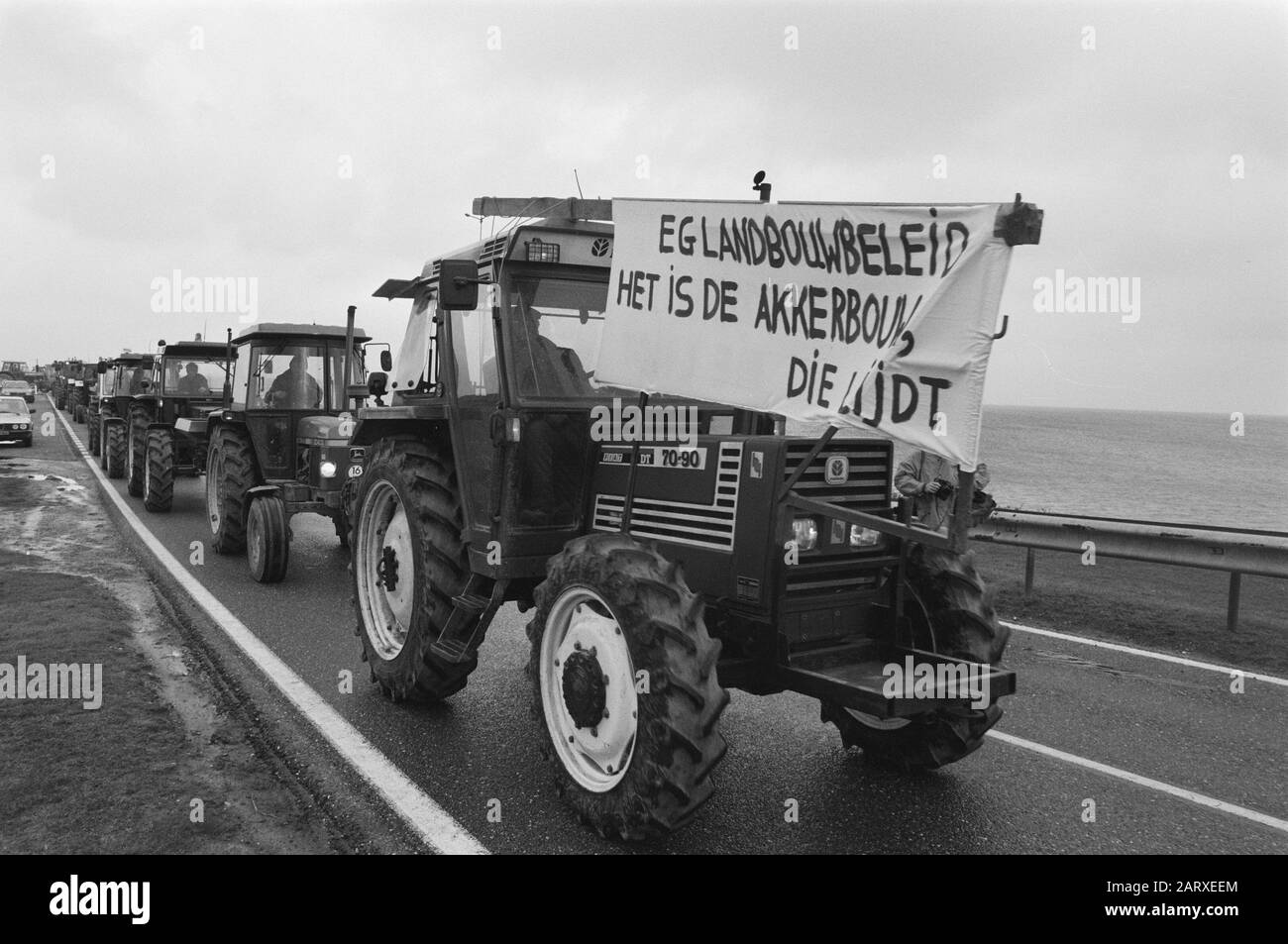 Acurbouwers veranstaltet eine Staffel-Tour mit Traktoren aus Protest gegen agrarpolitische Traktoren, die mit Bannern auf dem Afsluitdijk fahren Datum: 27. Februar 1989 Standort: Afsluitdijk Schlüsselwörter: Leuzen, Proteste, Banner, Traktoren Stockfoto