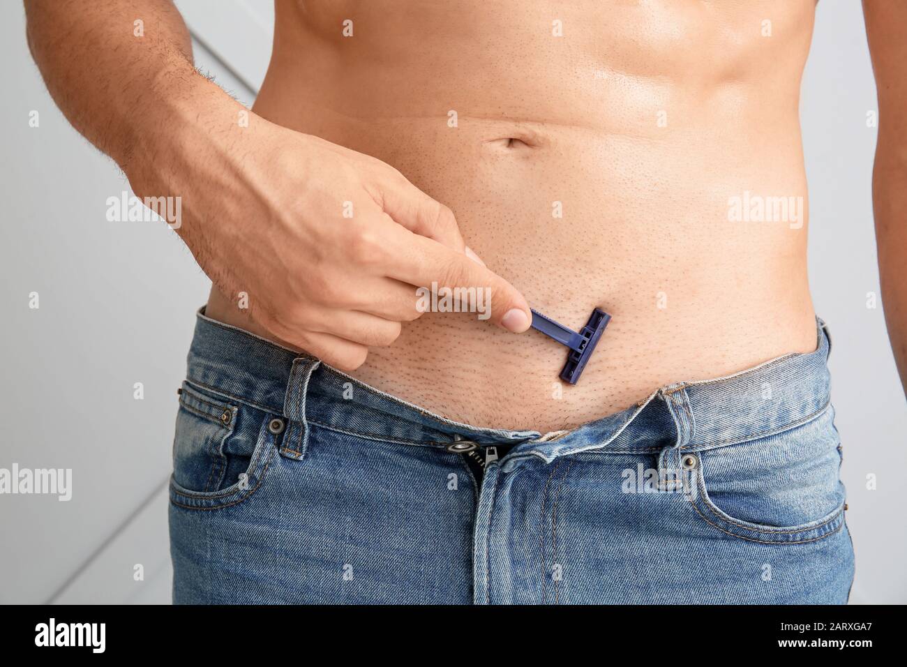 Gutaussehender junger Mann, der seinen Körper auf leichtem Hintergrund rasiert, in der Nähe Stockfoto