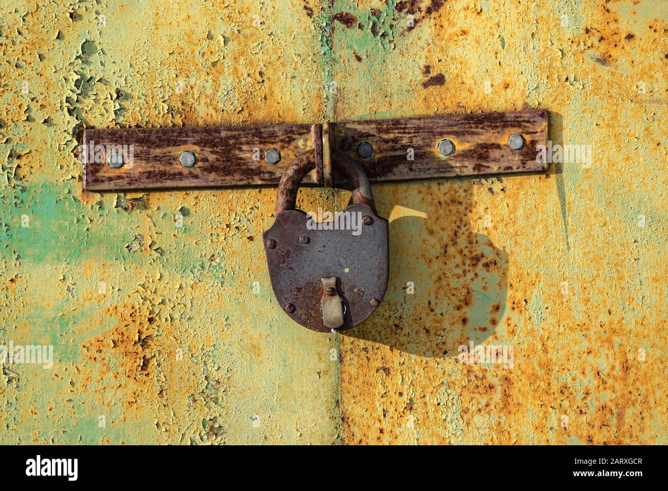 Ein altes braunes Schloss aus Eisen, das grün lackierte verkrustete Außentüren aus Metall sperrt. Blick auf einen sonnigen Tag. Die Lackschichten werden aufgeprallt. Mit Kopierbereich für Stockfoto