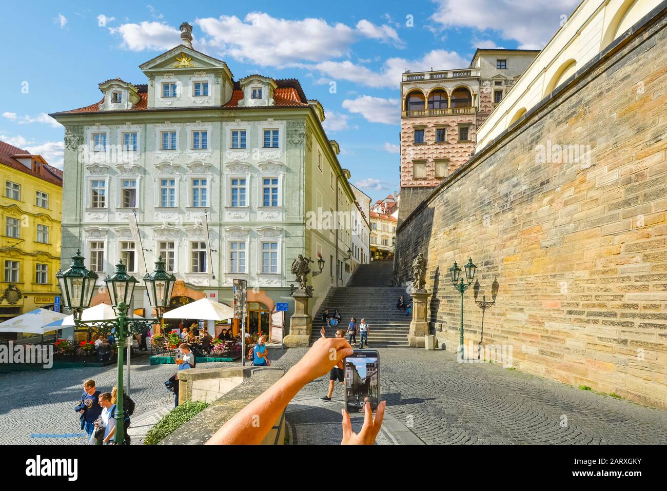 Ein Tourist nimmt ein Foto auf der Treppe zu der Prager Burganlage in der Tschechischen Republik als andere Besucher besichtigen und Essen in einem Café im Freien Stockfoto