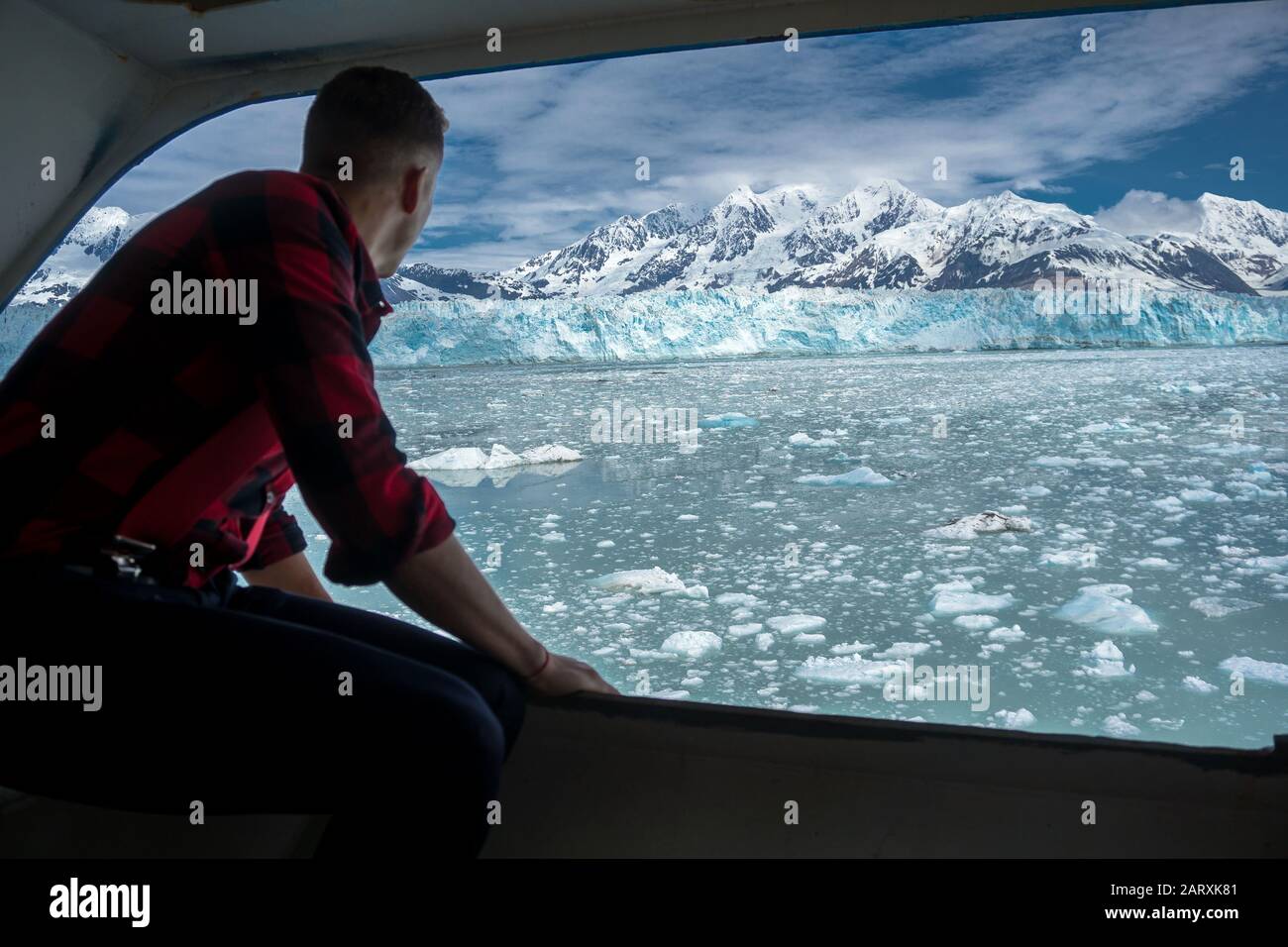 Der junge Mann blickt auf einen schönen Hubbard-Gletscher. Er ist auf einem Kreuzfahrtschiff in Alaska. Das Männchen trägt ein Holzfällerhemd und beobachtet den Eisberg. Stockfoto