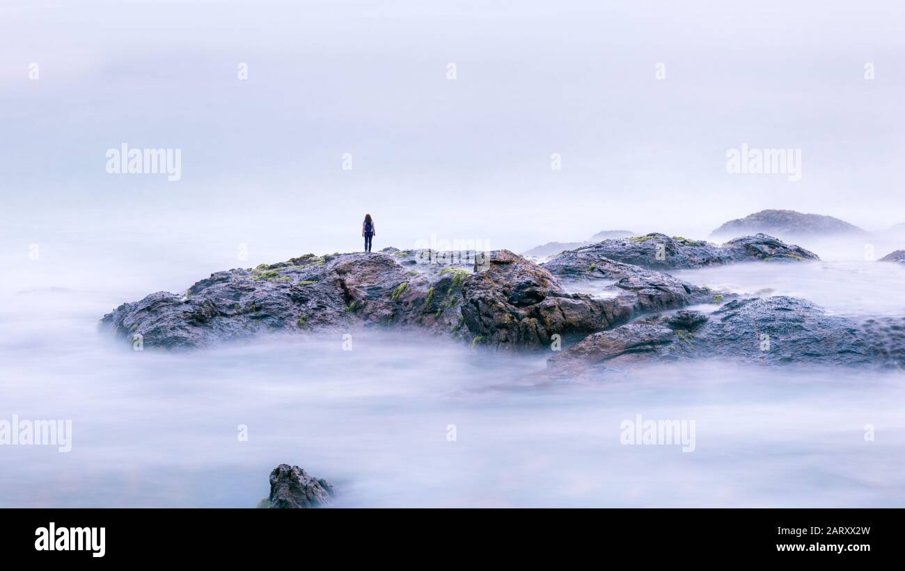 Magische Landschaft mit Einzelperson und surrealen Felsen im Meer. Lange Exposition von geheimnisvollen Ozeanen und Steinen. Fantastischer Blick auf Wasser wie Nebel, Nebel oder Wolken Stockfoto