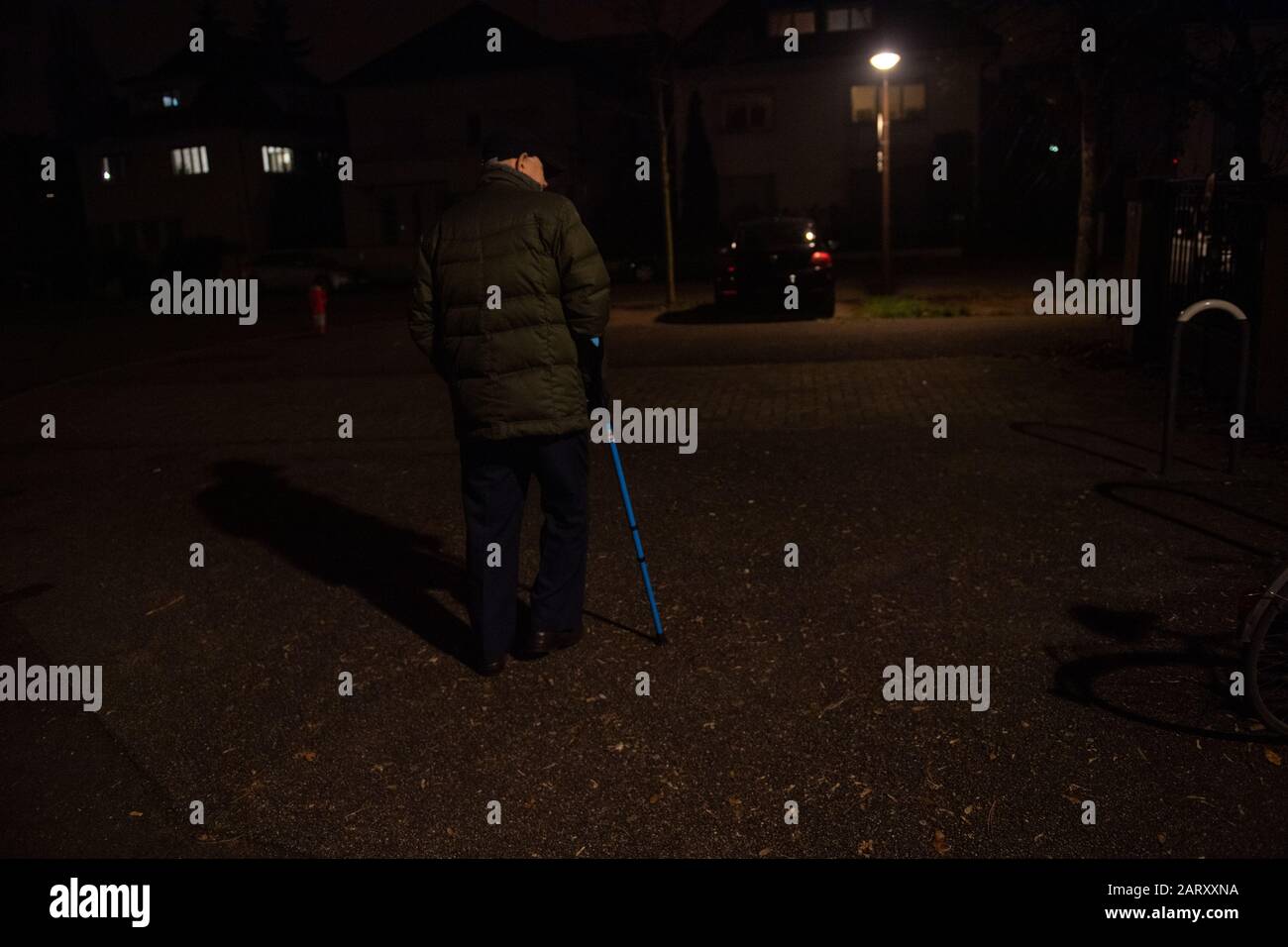 Einsamer älterer Mann, der nachts auf der französischen Straße mit einem Gehstock spazieren ging, um das Gleichgewicht mit blauem Teleskoprohr aus Aluminium zu erhalten medizinische Hilfe und Rehabilitation Stockfoto