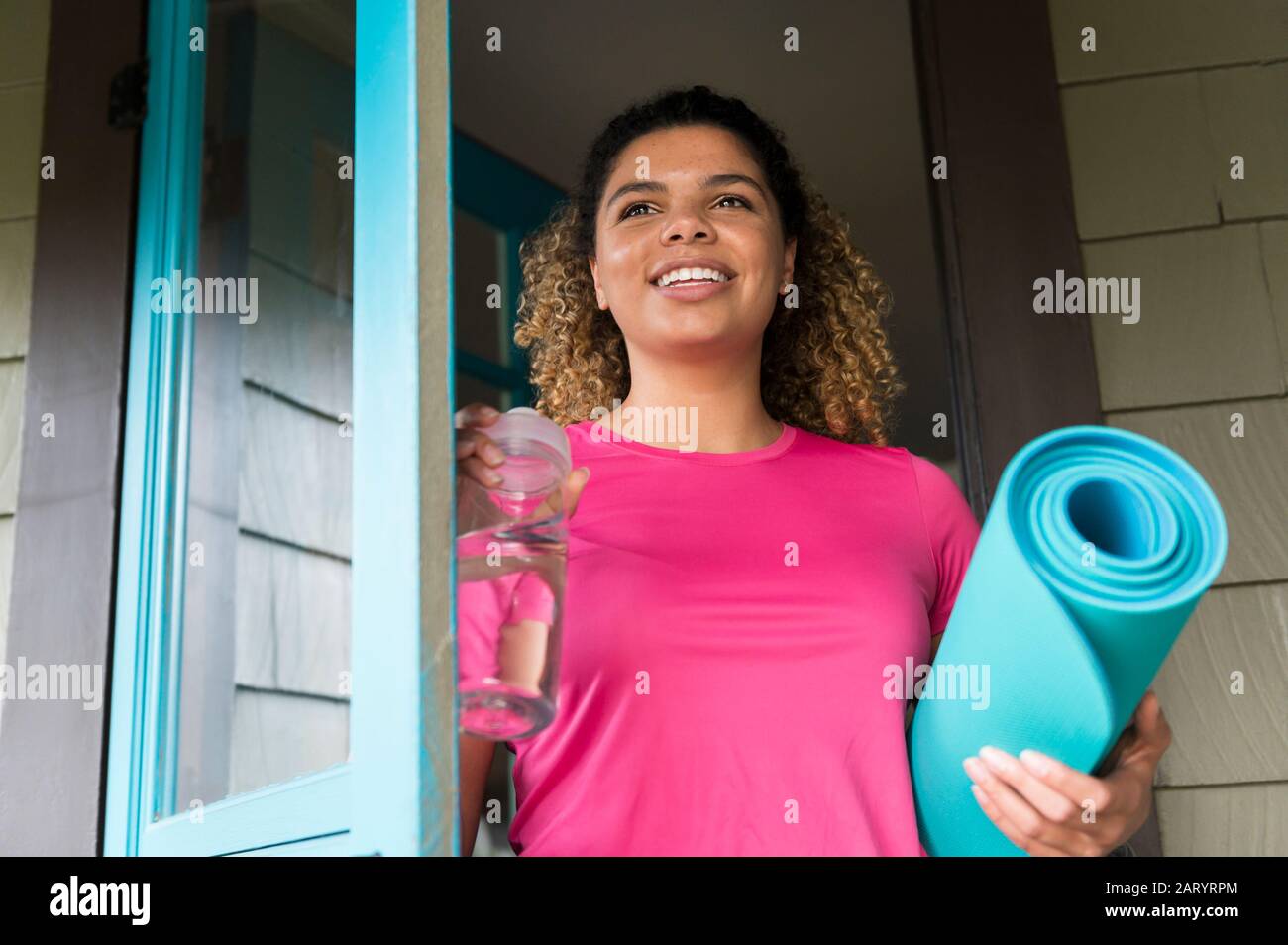 Lächelnde Frau mit Trinkflasche und Yogamatte Stockfoto
