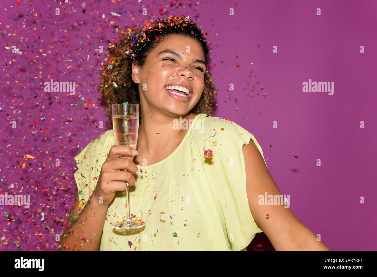 Lächelnde Frau hält Sektglas unter Konfetti Stockfoto