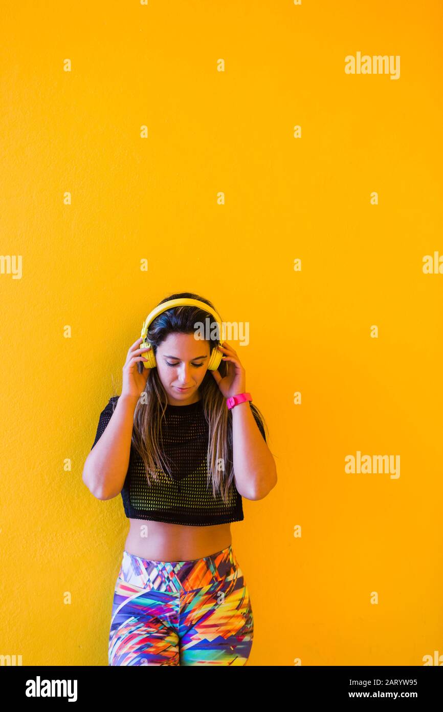 Frau trägt Kopfhörer an der gelben Wand Stockfoto