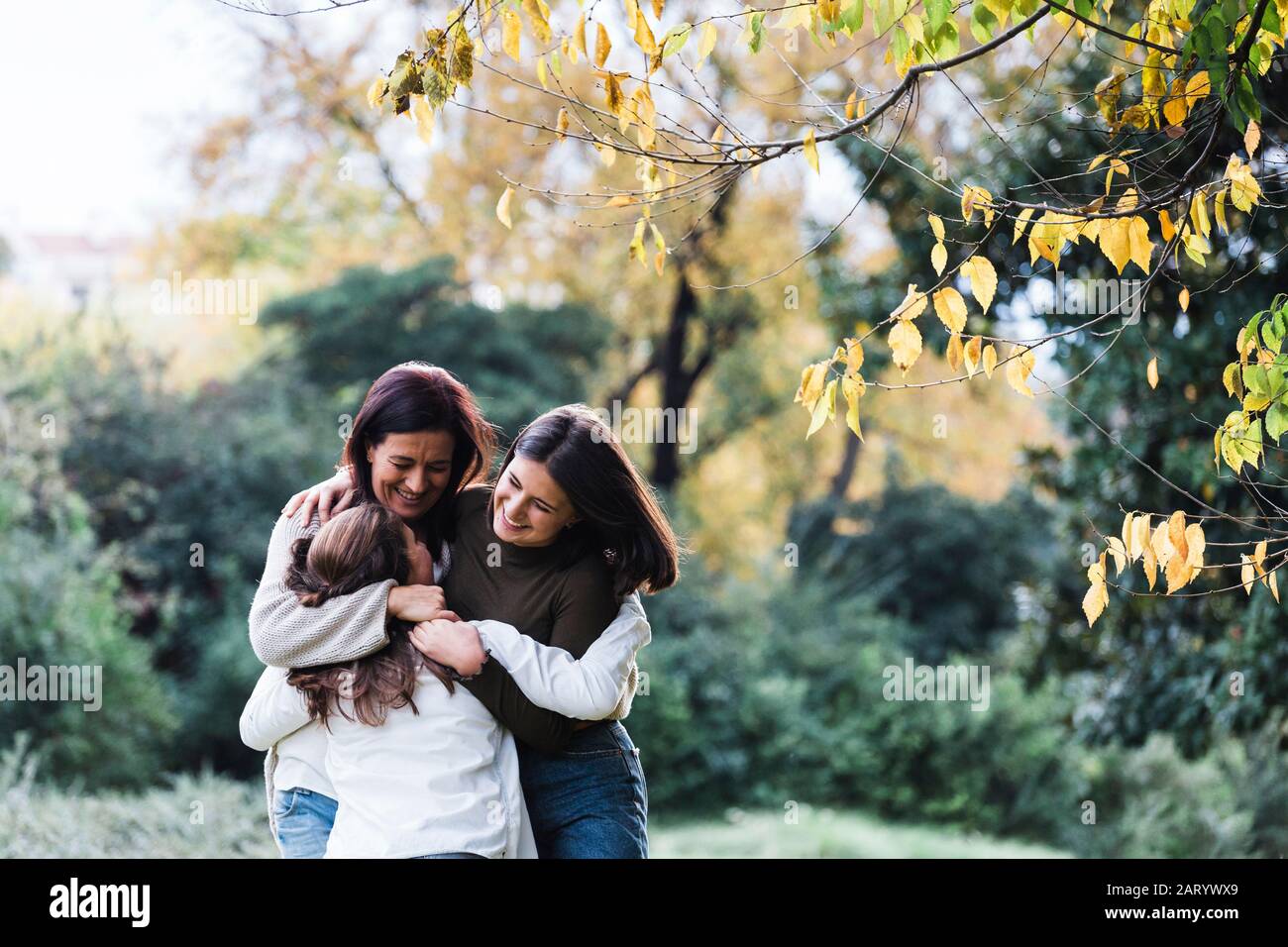 Mutter und Töchter lächeln und umarmen von Bäumen Stockfoto