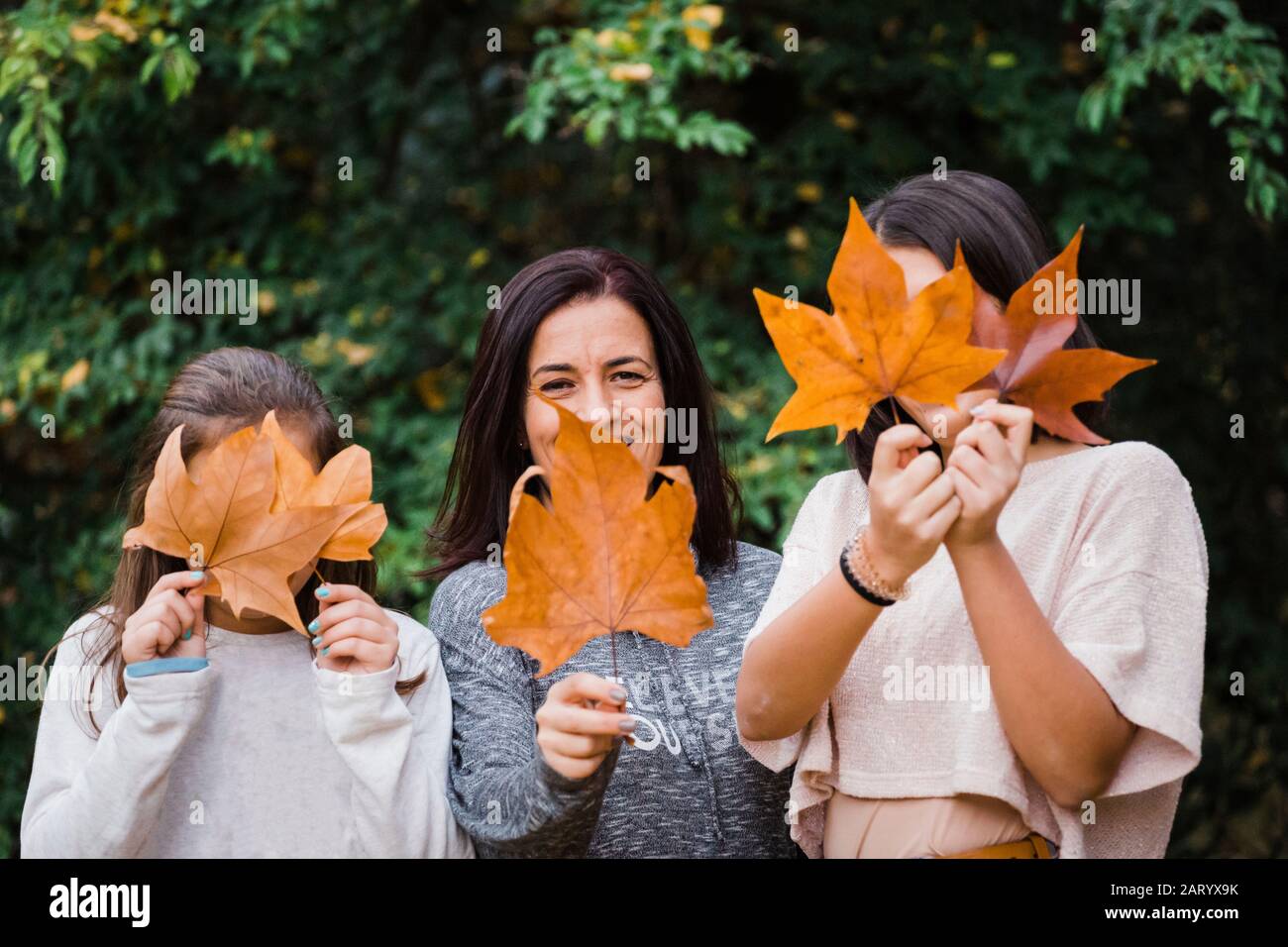 Mutter und Töchter verstecken sich hinter Herbstblättern Stockfoto