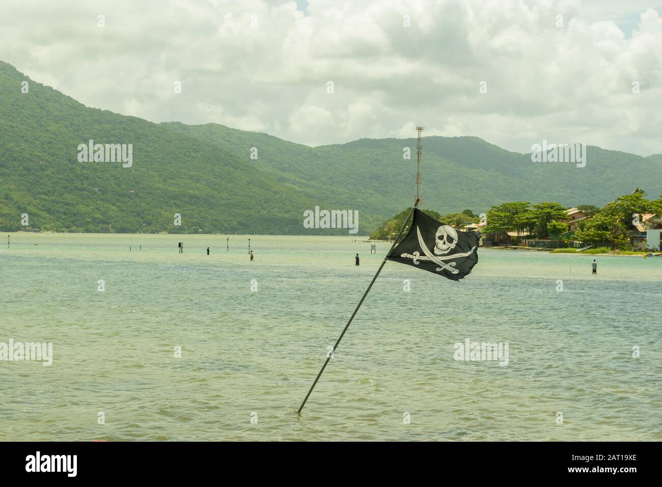 Piratenfahne flammend mit starkem Wind im See. Schöne Seenlandschaft mit Bergen im Hintergrund am sonnigen Tag. Stockfoto