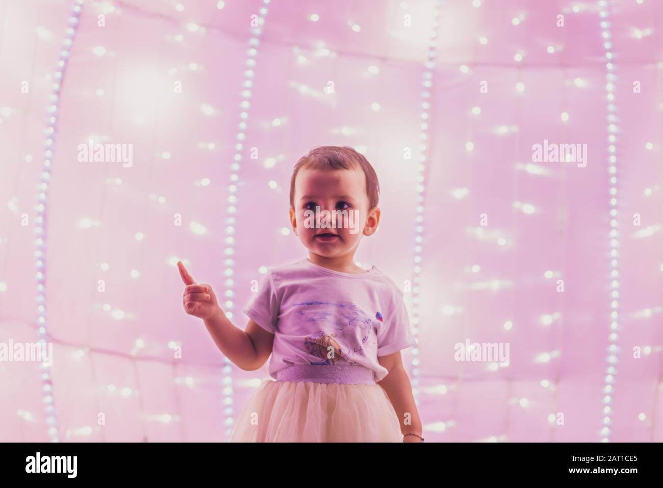 Ein süßes kleines Mädchen im rosafarbenen Outfit im rosafarbenen Coach mit leuchtenden LED-Lichtern im Dubai Glow Garden Stockfoto