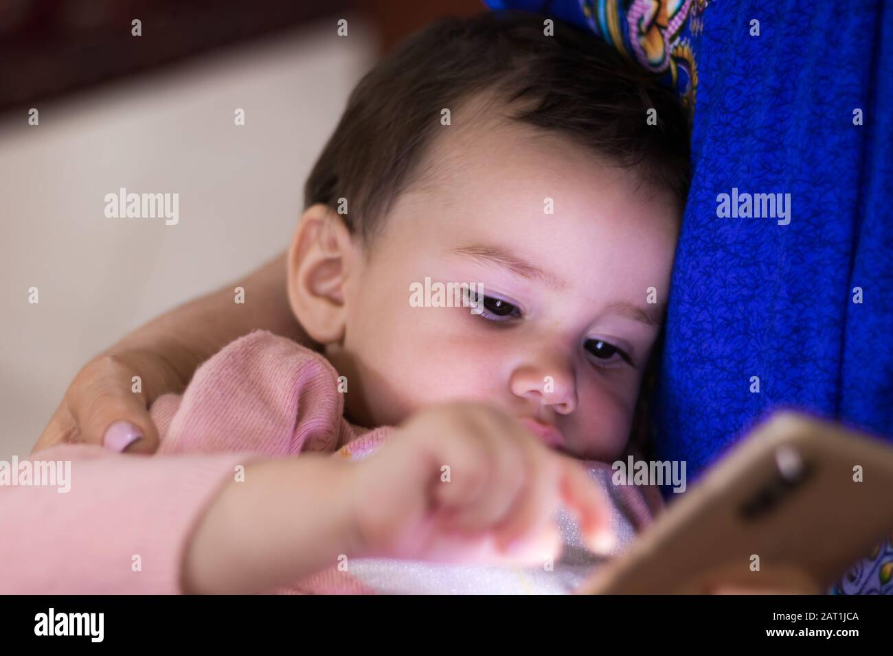 Ein süßes kleines Mädchen, das auf dem Smartphone Spiele spielt, während sie in den Runden ihrer Mutter sitzt Stockfoto