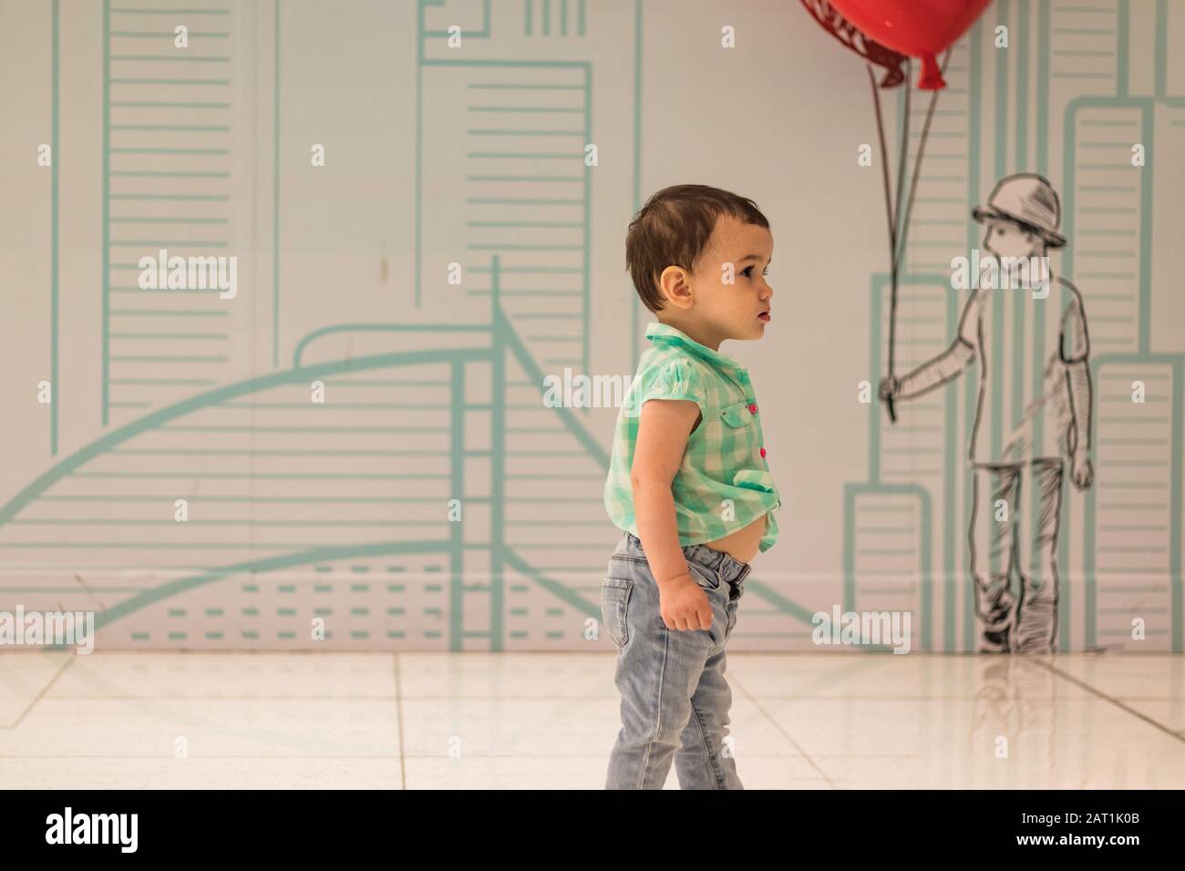 Ein süßes kleines Mädchen in der Dubai Mall mit der Zeichnung eines Jungen, der rote Luftballons im Hintergrund hält. Stockfoto