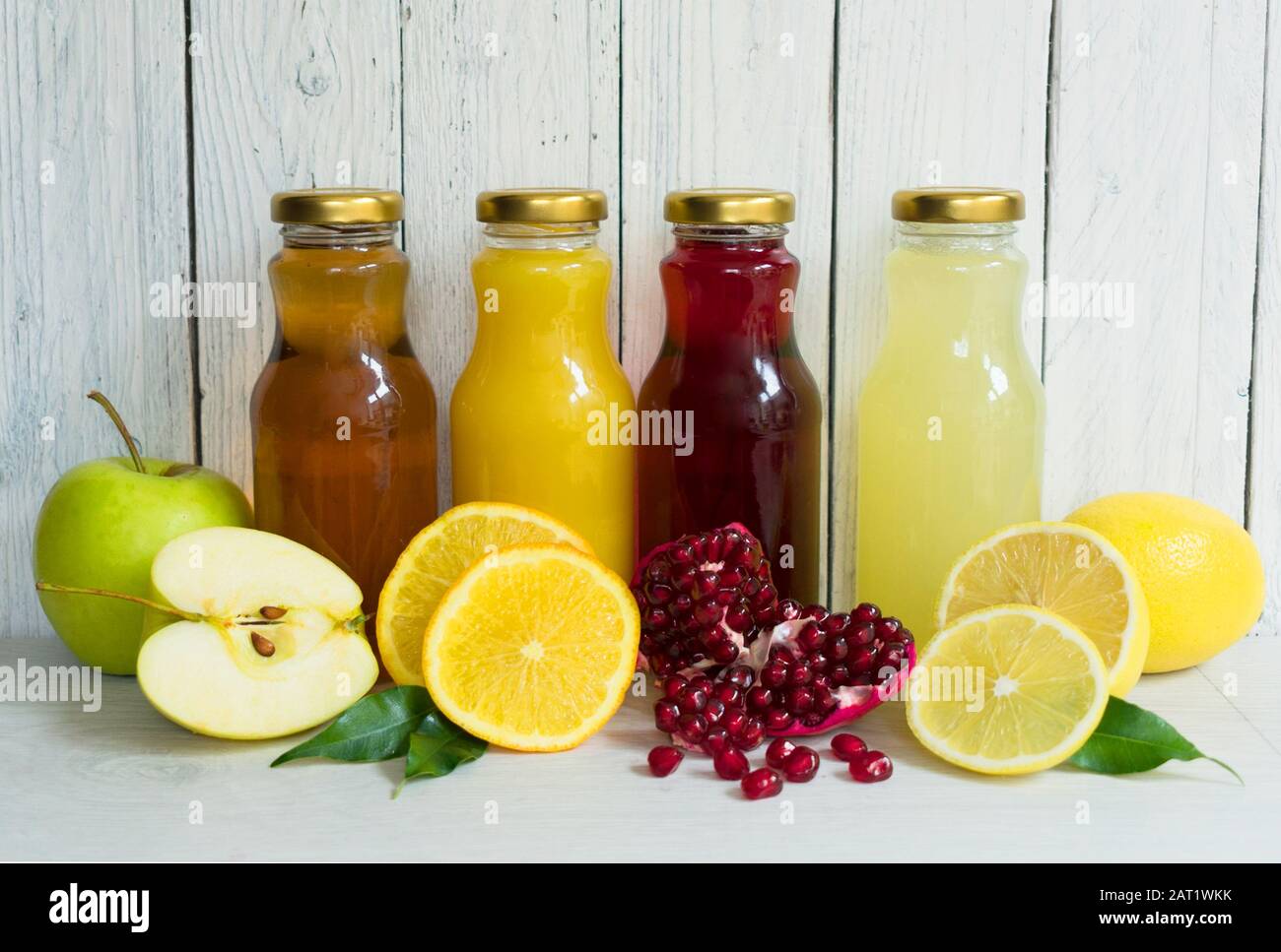 Vier Arten von Saft (Granatapfel, Apfel, Zitrone, Orangensaft) in Glasflaschen auf weißem Holz- Hintergrund. Stockfoto
