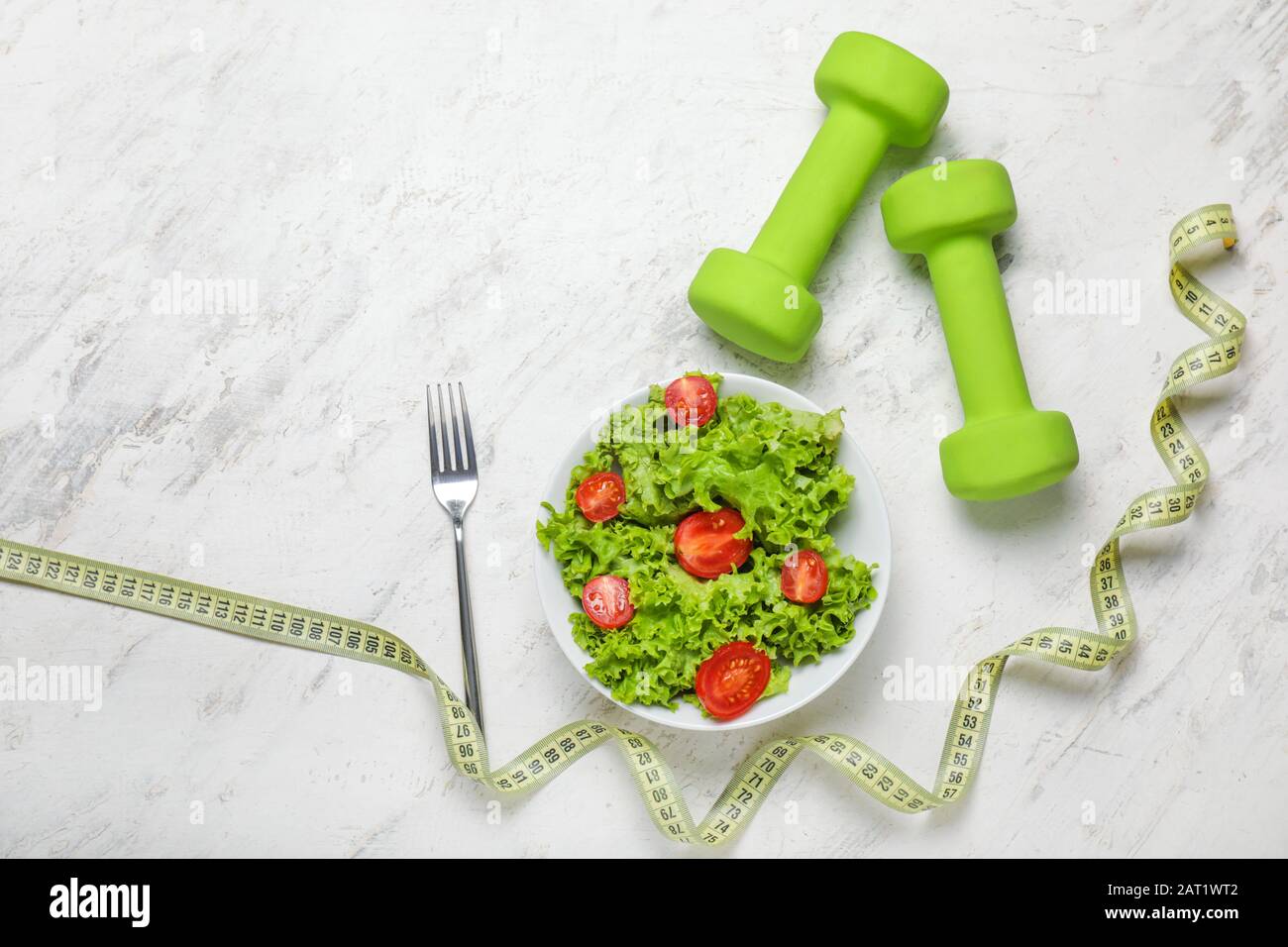 Gesunder Salat mit Messband und Hanteln auf hellem Hintergrund. Diät-Konzept Stockfoto