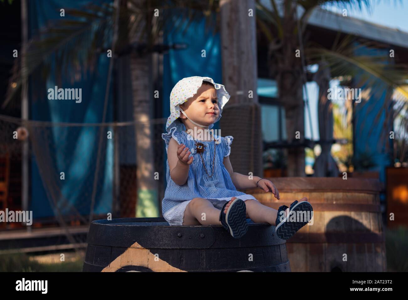 Ein süßes kleines Mädchen, das an einem sonnigen Tag auf einem Holzfass in Lammer, Dubai sitzt. Stockfoto