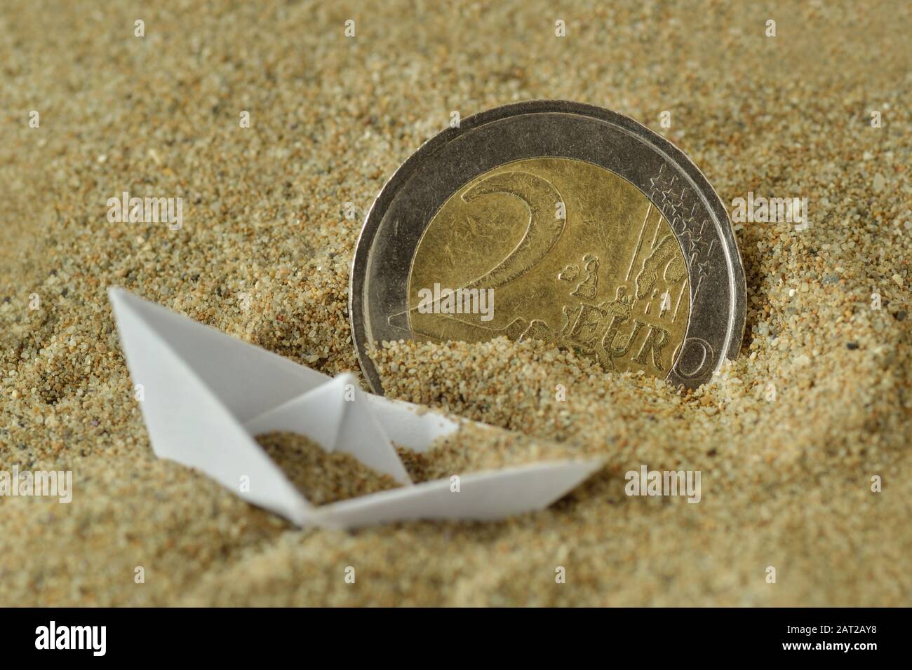 Euro-Münze und Papierboot sinken im Sand - Einwanderungskonzept Stockfoto