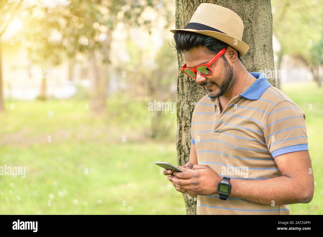 Fröhlicher inder, der sein Handy sieht und lächelt - Junger asiate, der online im Park im Freien textet - Neues Technologietrends Suchtkonzept - Krieg Stockfoto