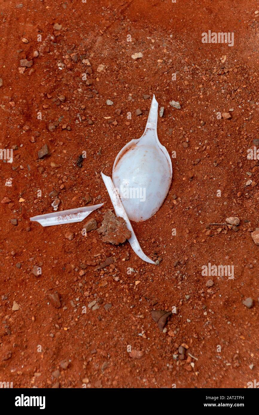 Nahaufnahme eines zerbrochenen weißen Plastiklöffels, der im sehr roten Sand sitzt Stockfoto