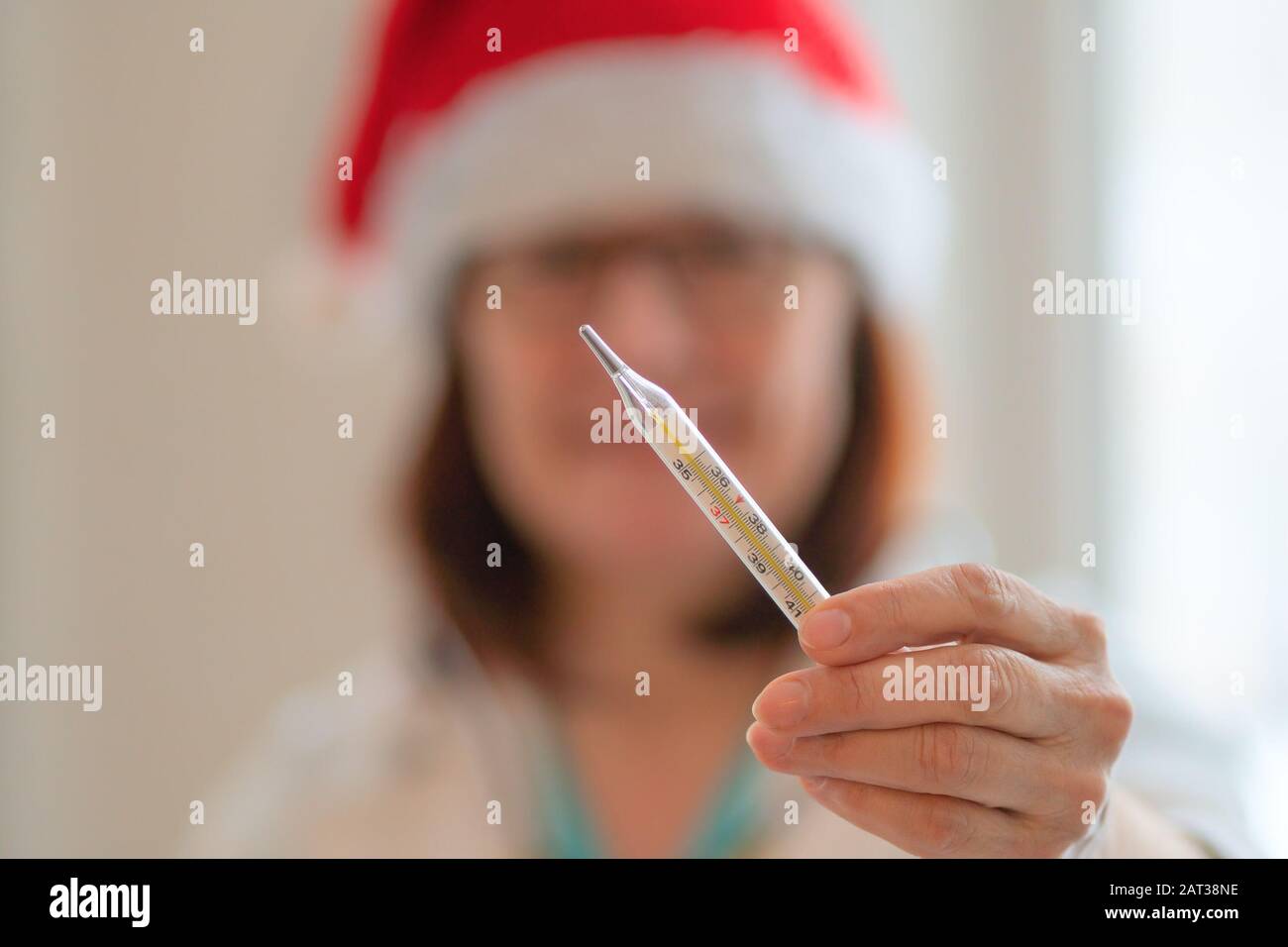 Lächelnder Arzt in weihnachtshut, der Thermometer in der Hand hält. Stockfoto