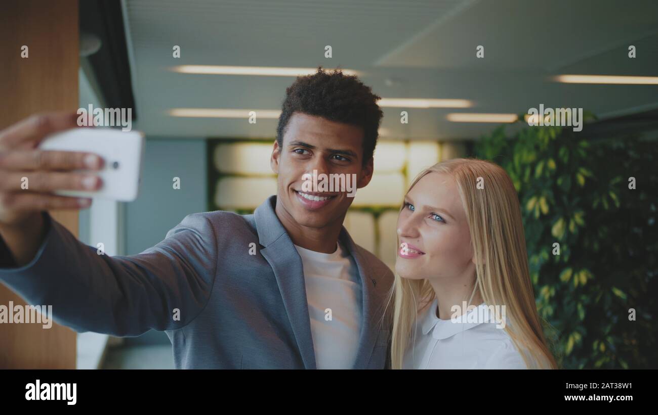 Fröhliche schwarzer Mann mit Lachen, blonde Frau, die selfie mit Smartphone in modernen Büro Spaß haben. Stockfoto