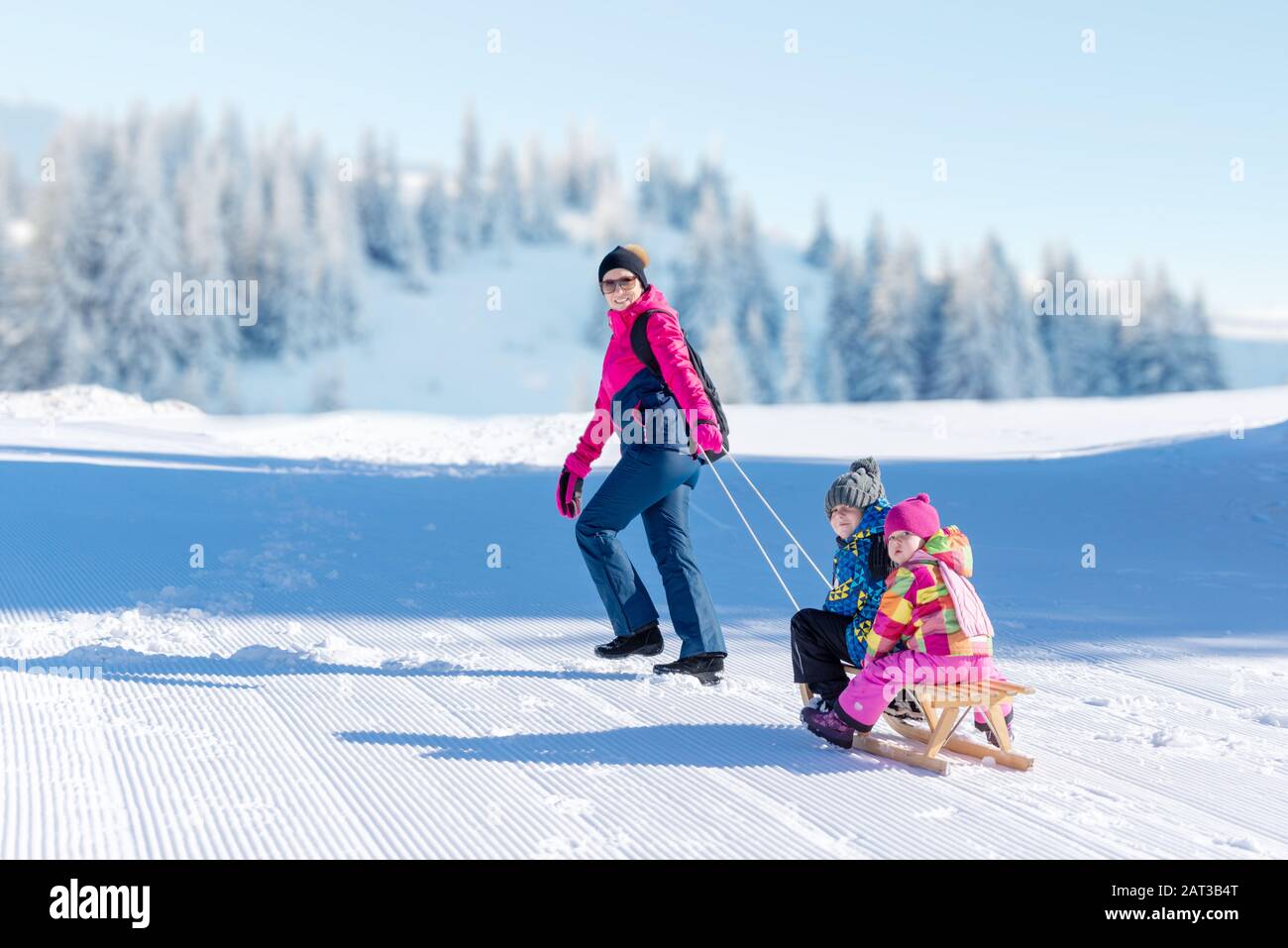 Mutter zieht den Schlitten mit dem Jungen und dem Mädchen. Spielkonzept für Schnee- und Winterurlaub Stockfoto