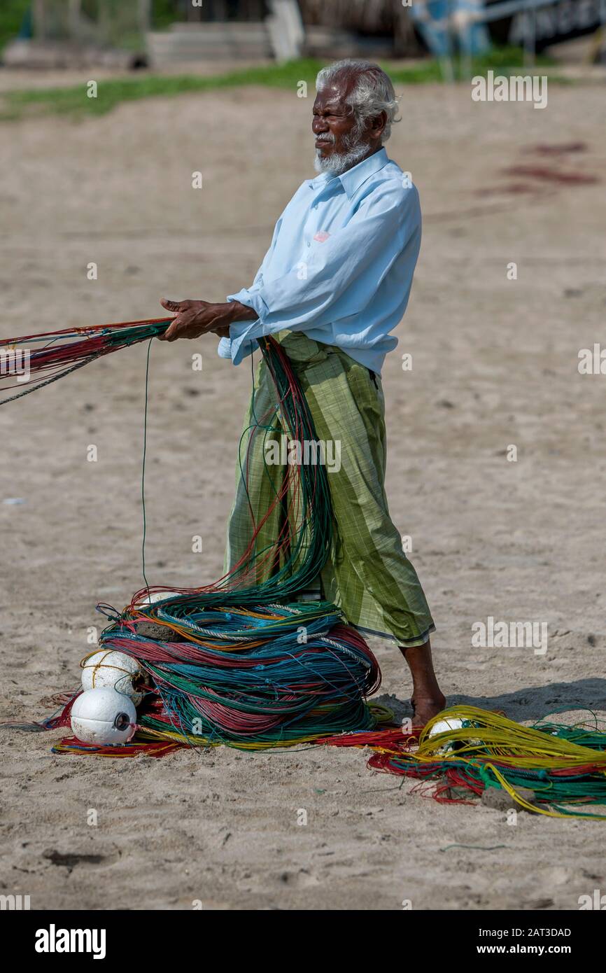 Ein lokaler Fischer hilft am frühen Morgen, die bunte Linie eines Fischerntnetzes auf den Strand von Uppuveli in Sri Lanka zu rollen. Stockfoto
