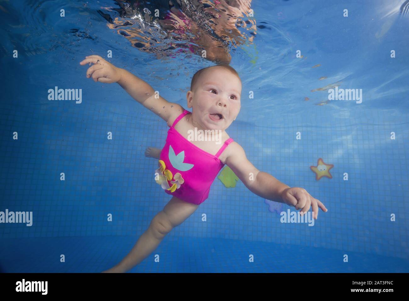 Kleines Mädchen in einem rosafarbenen Badeanzug lernt, unter Wasser im Pool zu tauchen Stockfoto