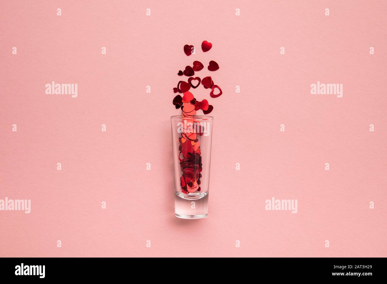 Valentinstagsaufnahmen. Glas mit Herzkonfetti auf pastellrosa Hintergrund Stockfoto