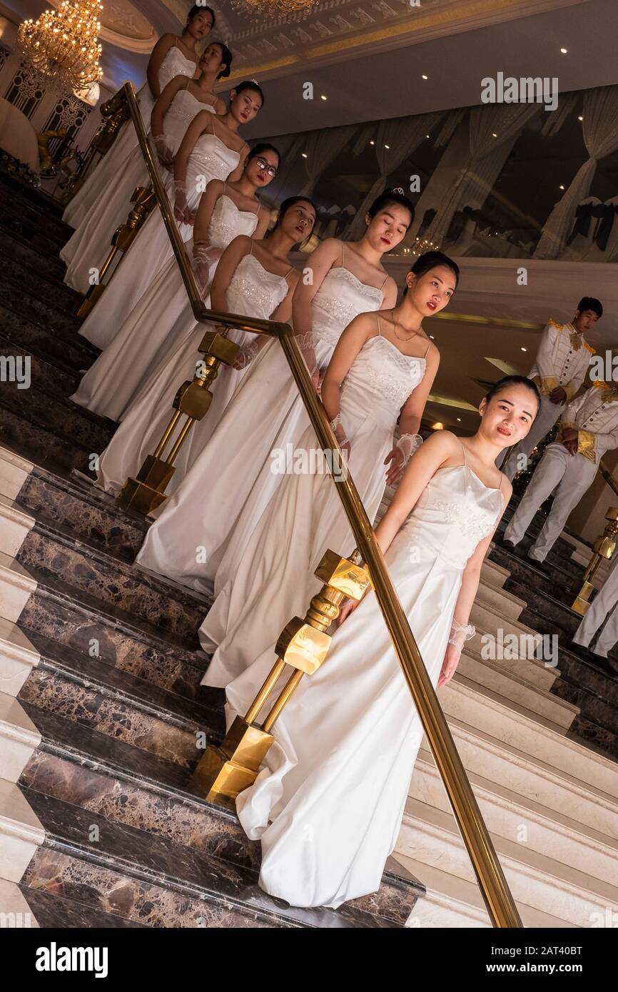 Junge Frauen in langem weißen Kleid auf der Treppe warten auf Brautpaar für Hochzeitsempfang, Ho-Chi-Minh-Stadt, Vietnam Stockfoto
