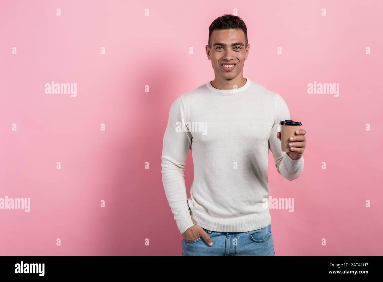 Halblanges Porträt des glücklichen Mulatto man, der ein Glas Kaffee aus Papier hält, das vor einem rosafarbenen Hintergrund steht.- Bild Stockfoto