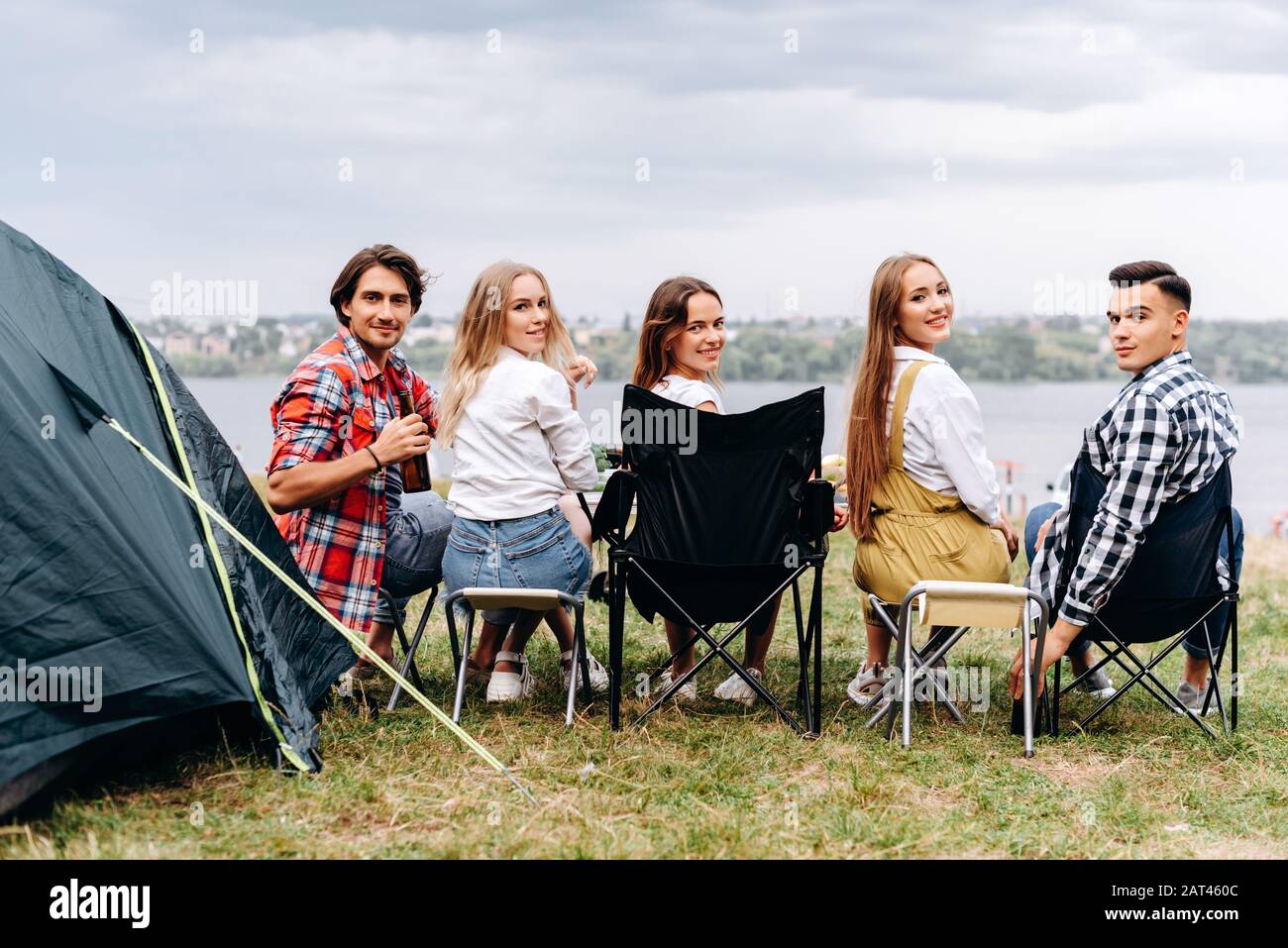 Eine Gesellschaft von Freunden hat eine lustige Zeit auf dem Camping. Sie sitzen eine halbe Umdrehung. - Rückansicht Stockfoto