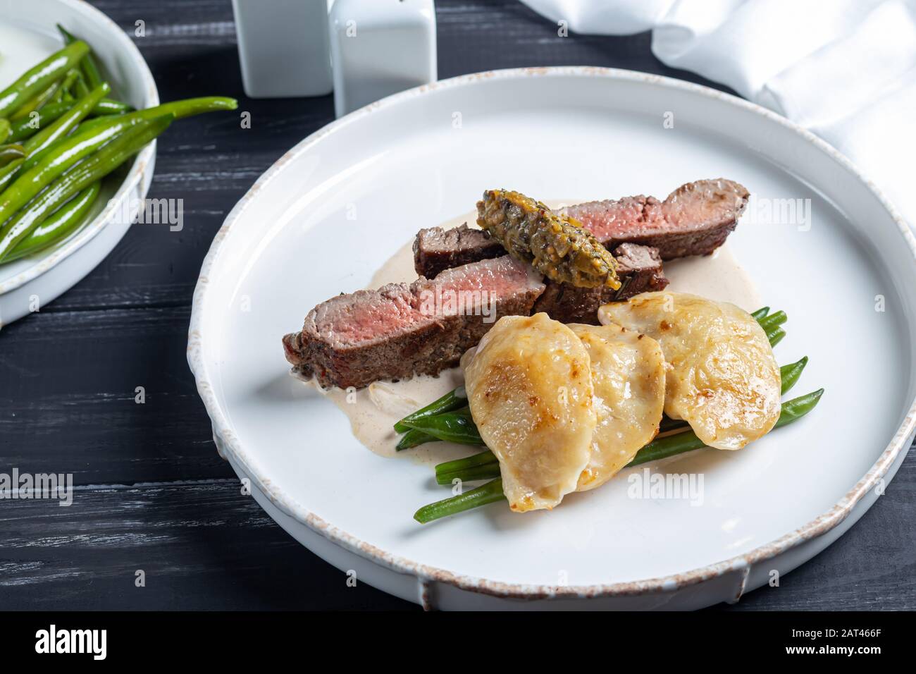 Gegrilltes Fleischsteak New York Striploin. Knödel mit Steinpilzen in Spargel-Trüffelsoße. Auf einer Holztafel auf dunklem Grund. Kopierbereich Stockfoto