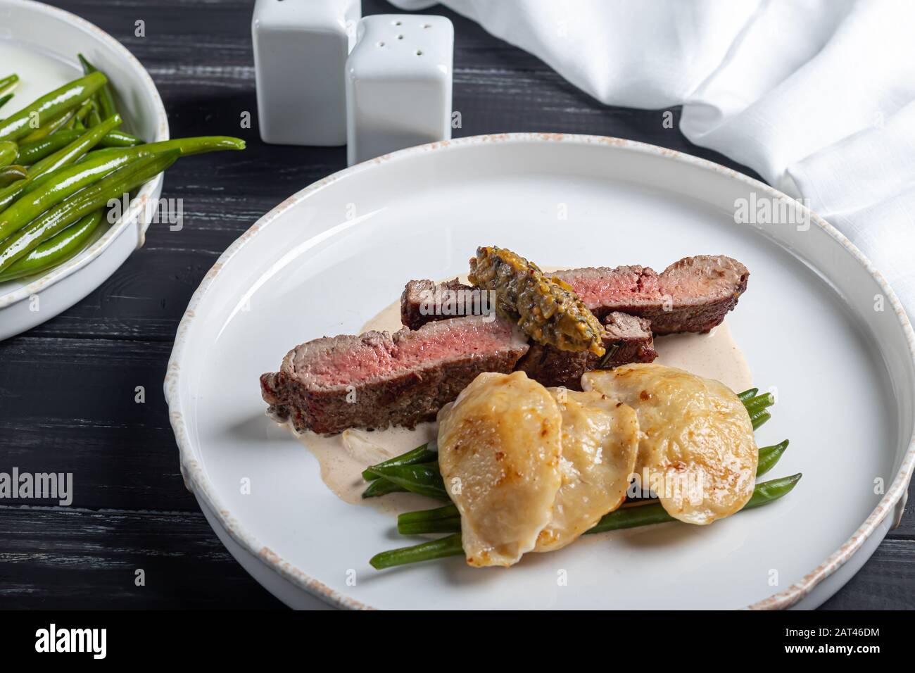 Gegrilltes Fleischsteak New York Striploin. Knödel mit Steinpilzen in Spargel-Trüffelsoße. Auf einer Holztafel auf dunklem Grund. Kopierbereich Stockfoto