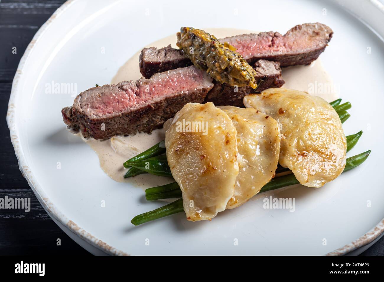 Gegrilltes Fleischsteak New York Striploin. Knödel mit Steinpilzen in Spargel-Trüffelsoße. Auf einer Holztafel auf dunklem Grund. Kopierbereich Stockfoto