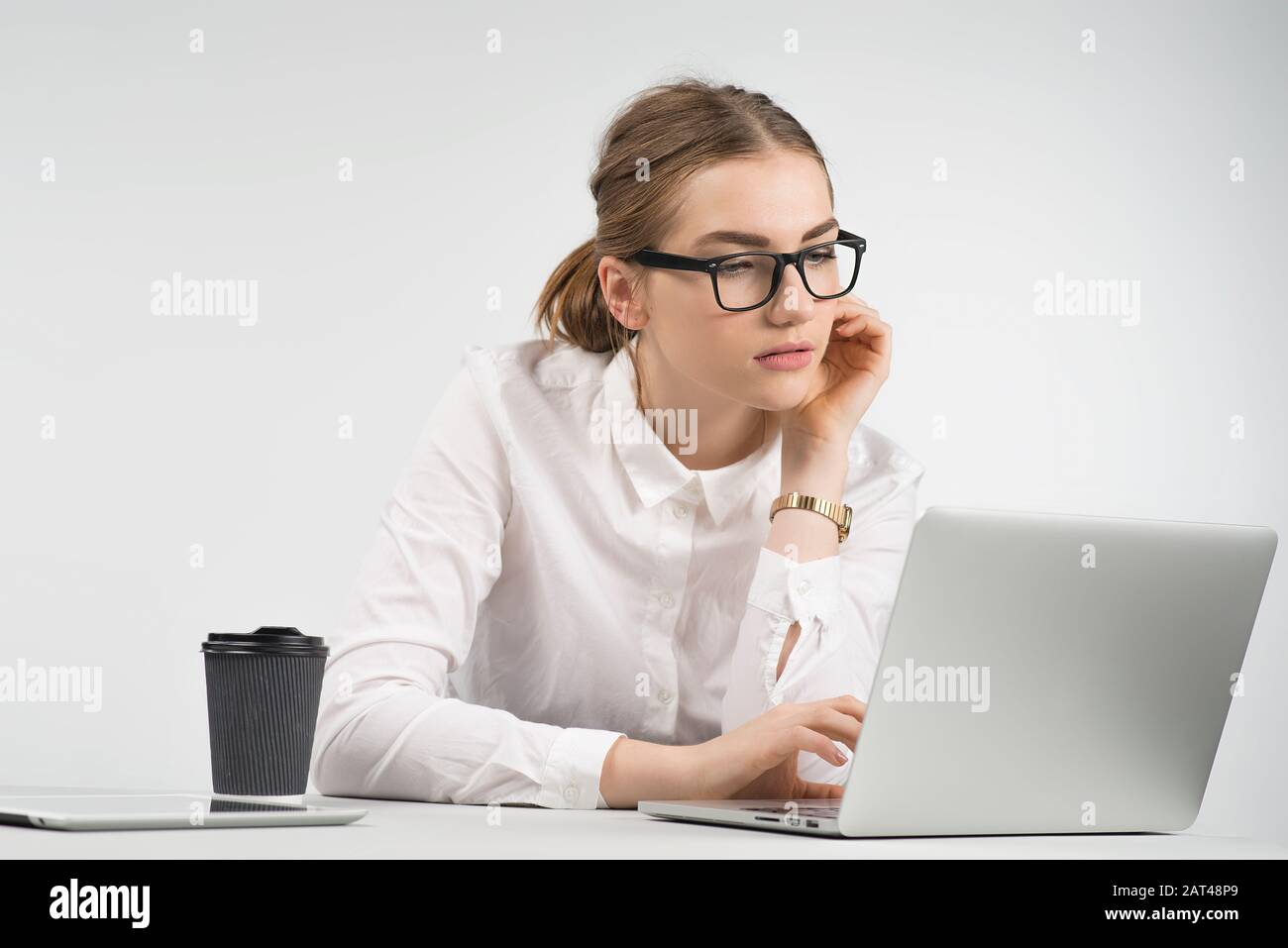 Intelligente Geschäftsfrau sitzt und arbeitet vorsichtig hinter einem Laptop mit einer Tasse Kaffee und einem ipad auf dem Tisch Stockfoto