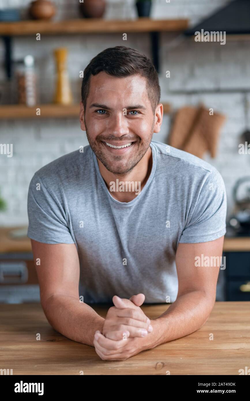 Ansehnlicher Mann sitzt lächelnd auf dem Tisch und blickt auf die Kamera.- Bild Stockfoto