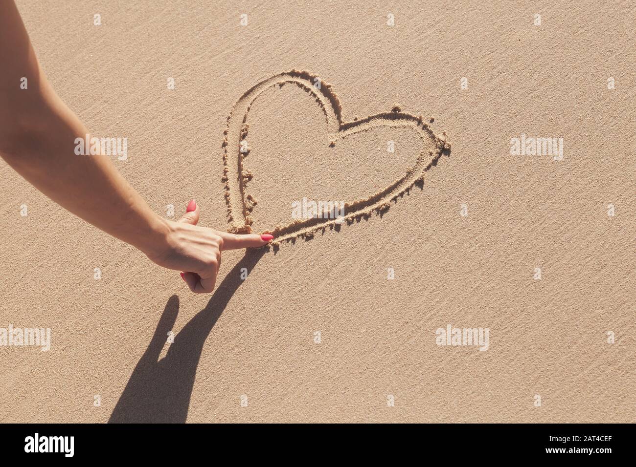 Mädchen Hand zeichnet ein Herzschild auf einem Küstensand, eine romantische Weihnachtsmetapher Stockfoto