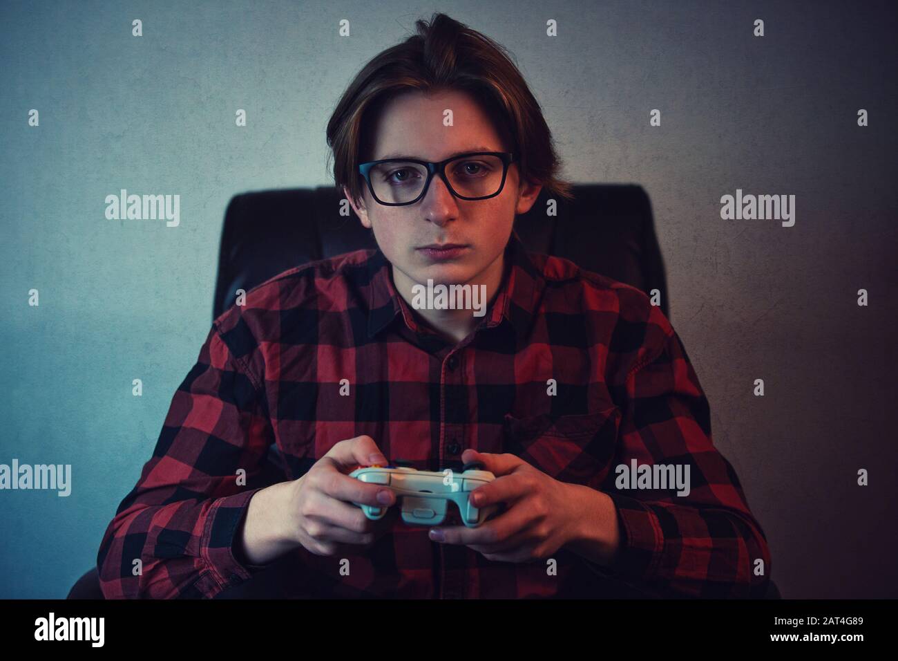 Ein ernsthafter Junge, der am späten Abend Videospiele spielt, sitzt im Sessel in einem dunklen Raumhintergrund. Vorsatz Teen Mann, der ein Joystick-Konsole-Loo hält Stockfoto