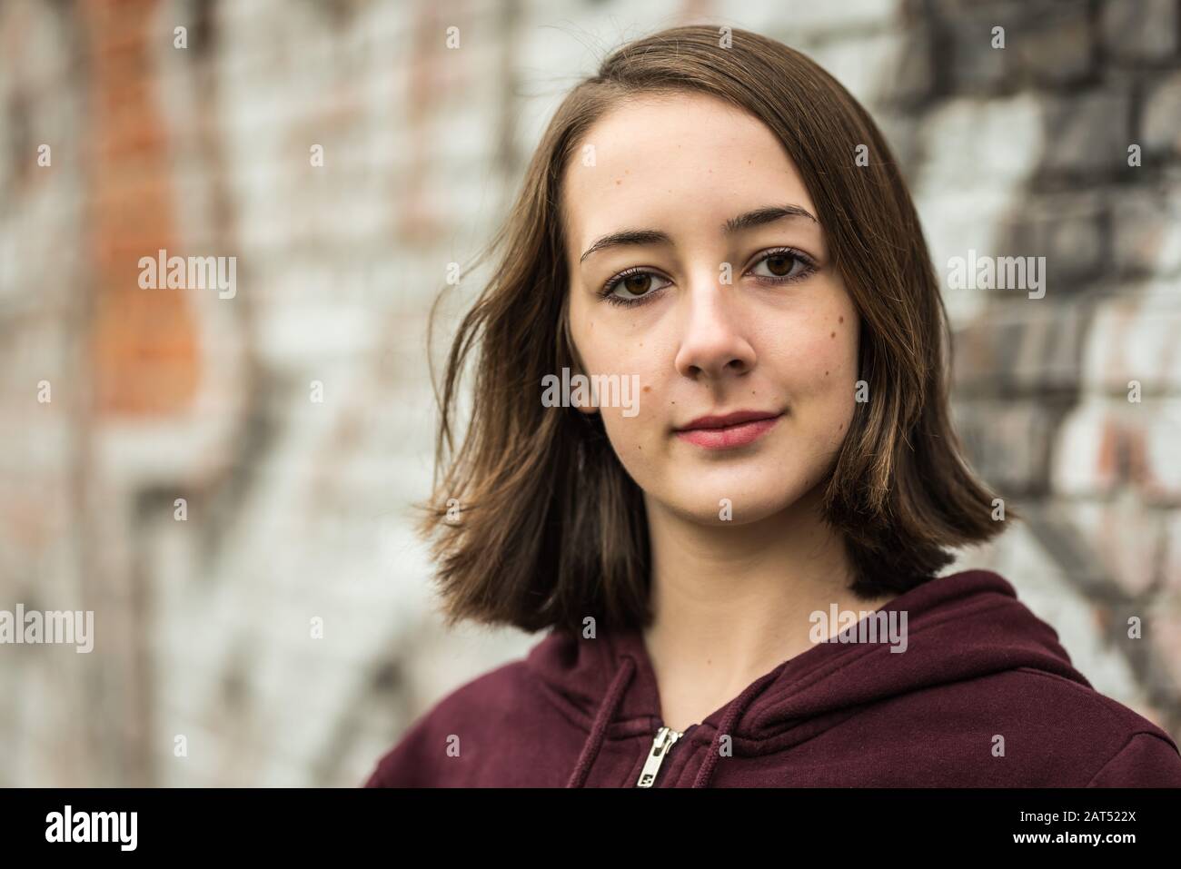 Kopfschuss eines 17 Jahre alten College-Mädchens mit einem Hoodie, das gegen eine raue Wand posiert Stockfoto