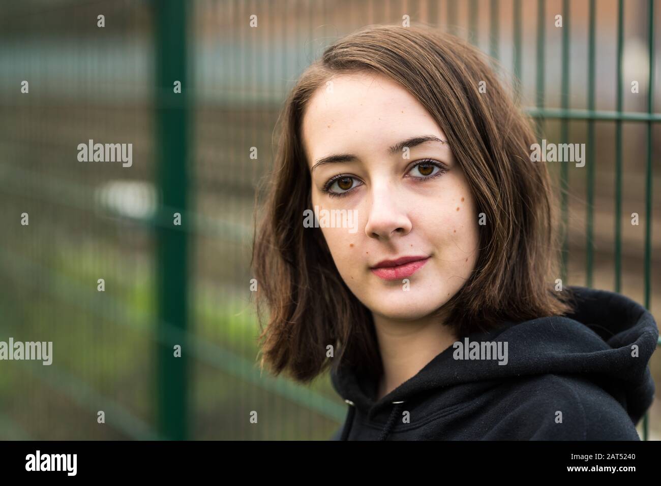 Kopfschuss eines 17 Jahre alten College-Mädchens mit einem Hoodie, das gegen eine raue Wand posiert Stockfoto