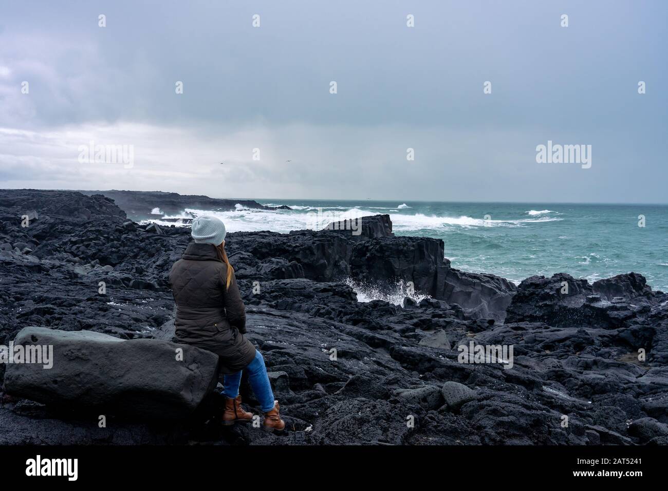 Frau, die auf einem Felsen sitzt und dabei die Macht des Ozeans auf der seeast reykjanes in Island beobachtet Stockfoto