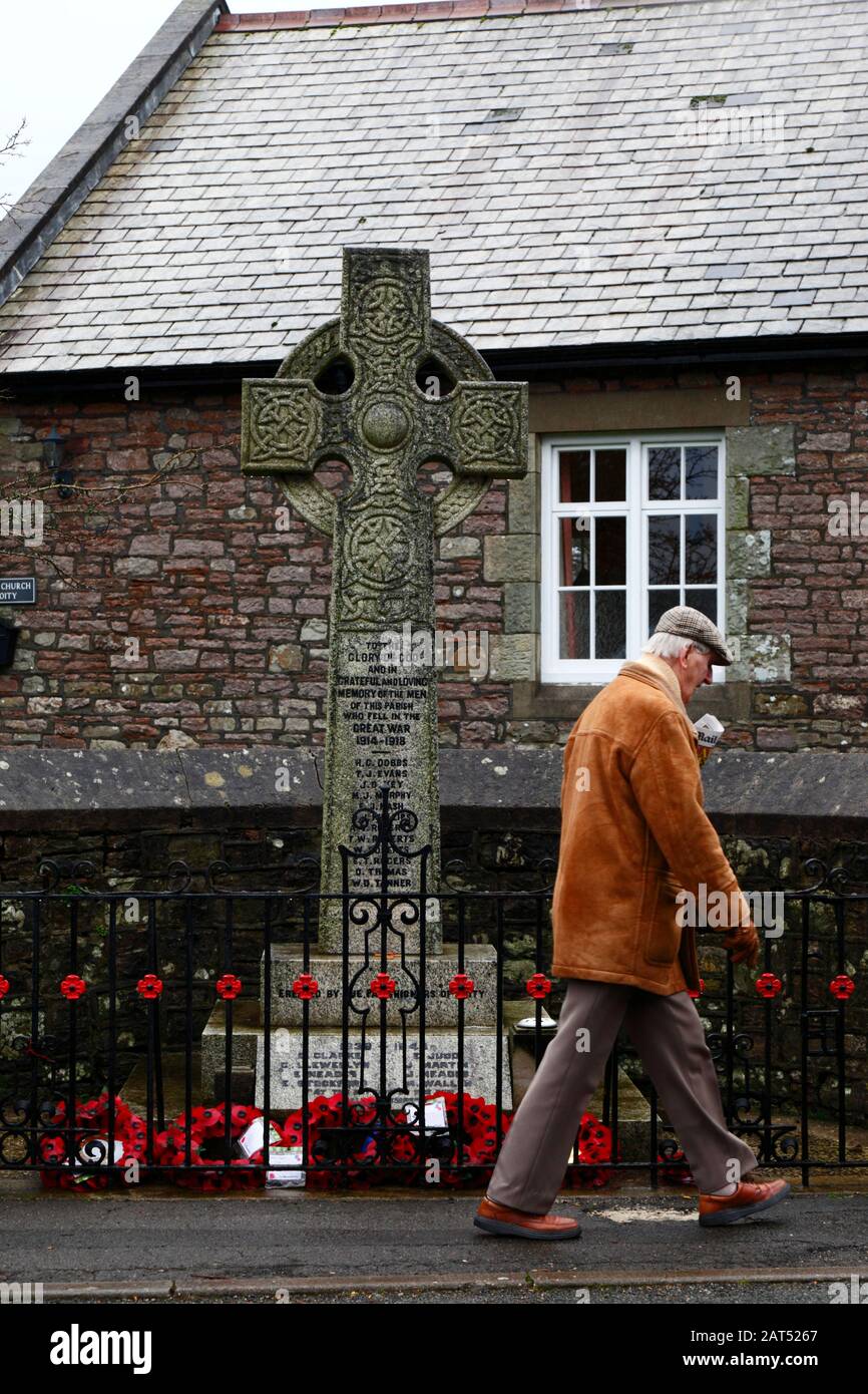 Mann, der an Mohnkränzen am Sockel des Kriegsdenkmals in Coity Village, Mid Glamorgan, Wales, Großbritannien vorbeiläuft Stockfoto